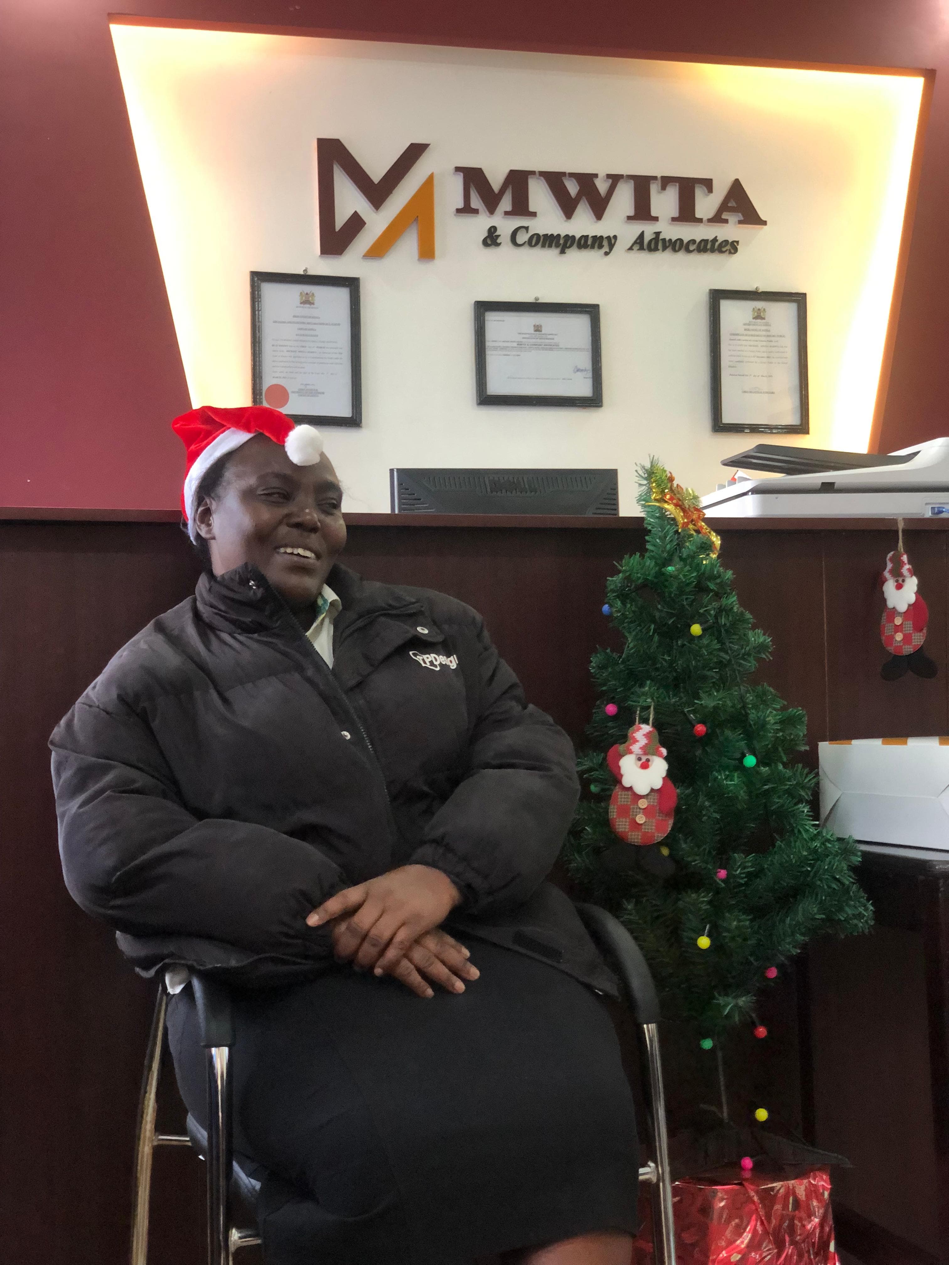 A member of the Mwita & Co. team in a Santa hat at the firm's reception, beside a decorated Christmas tree.