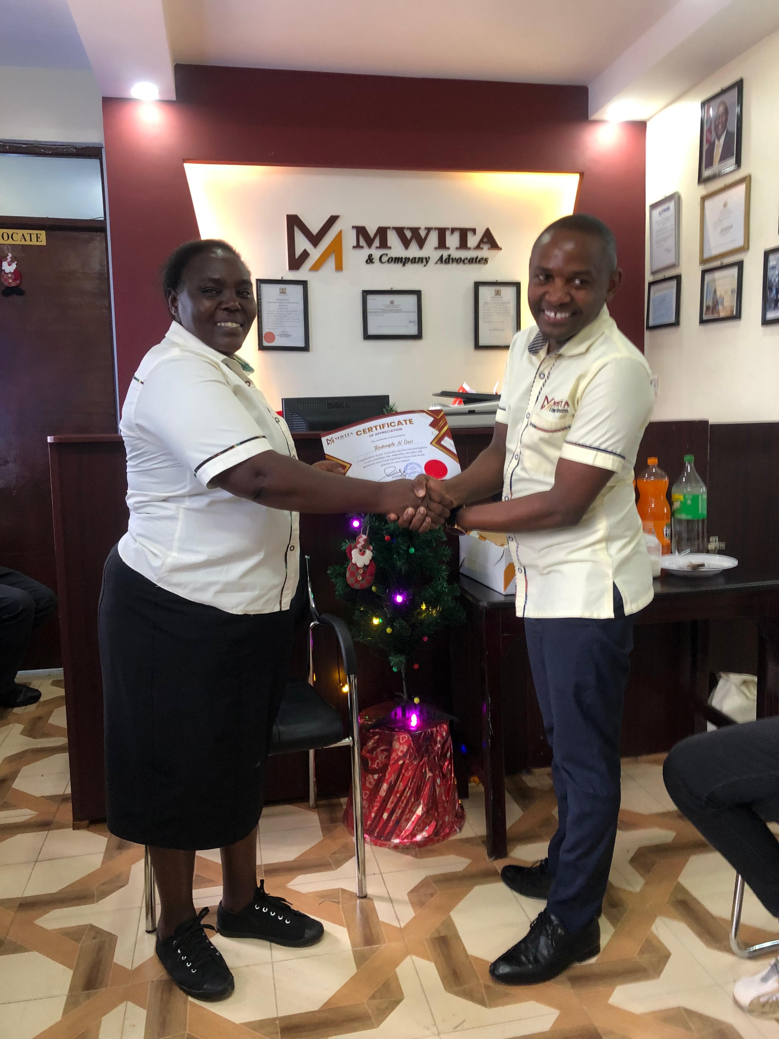 A Mwita & Co. certificate being presented in the firm's reception area beside a Christmas tree.