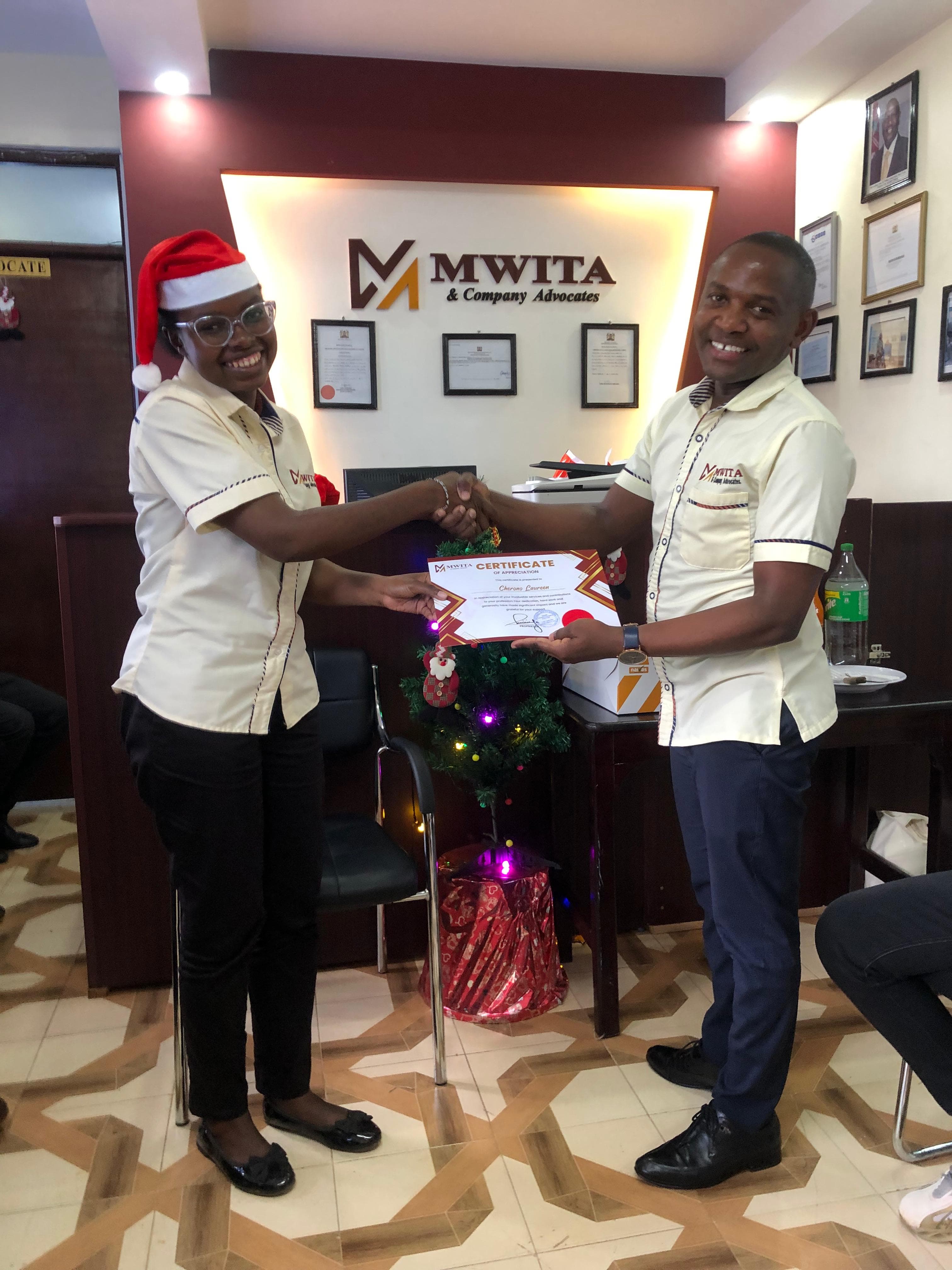 A smiling Mwita & Co. team member receiving a certificate in the firm's reception area.