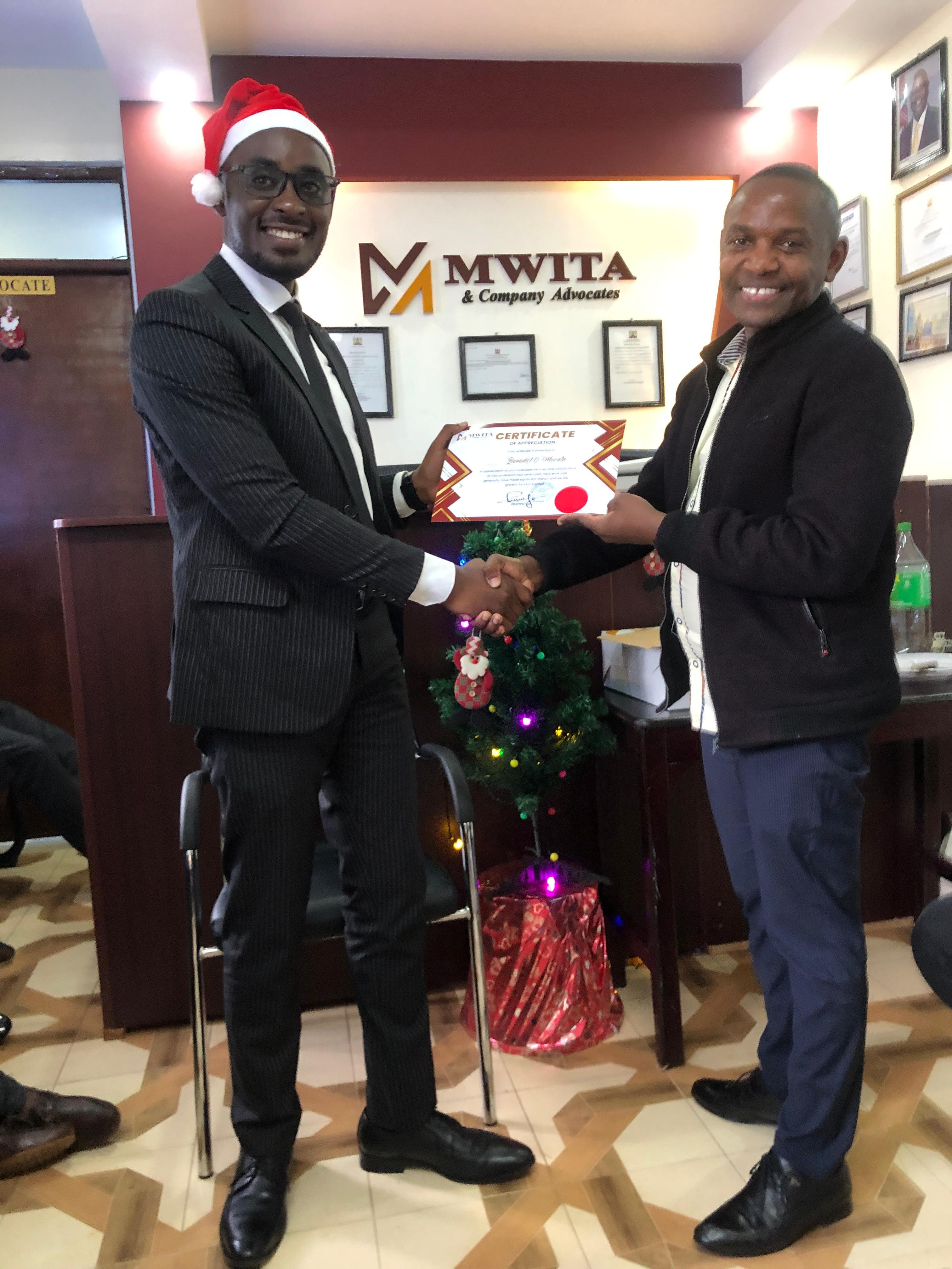 A Mwita & Co. advocate presenting a certificate during a festive office celebration.